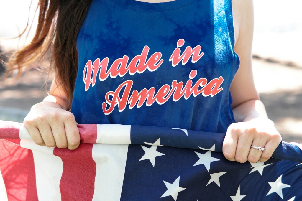 An American wearing a "Made in America" t-shirt and holding an American flag.