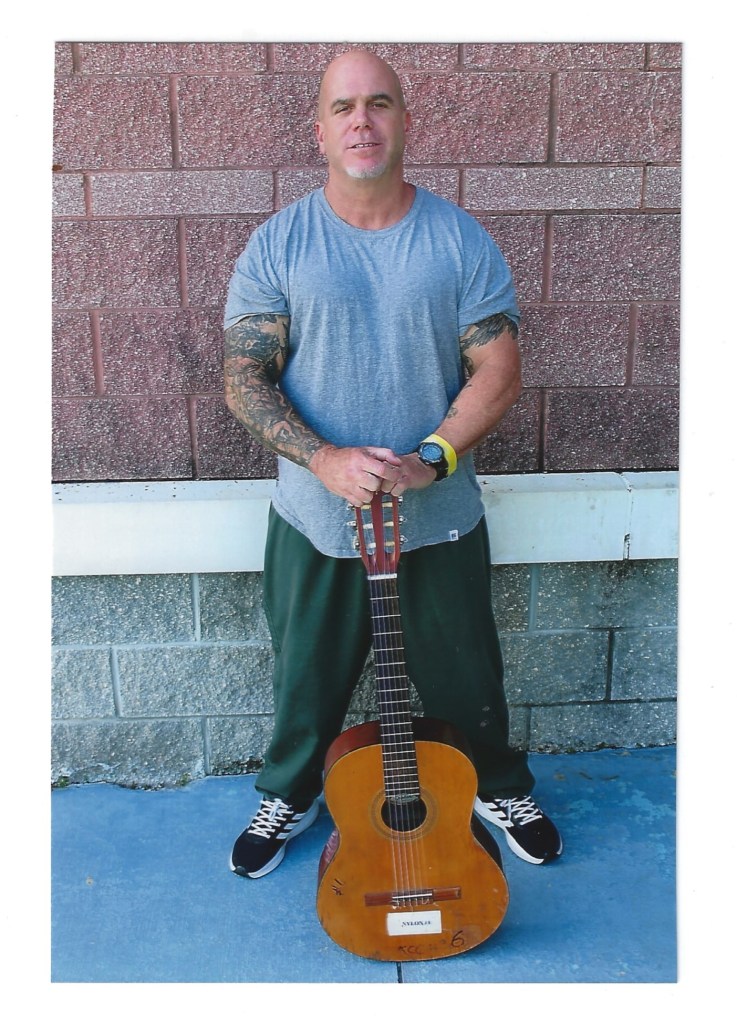 Photo of author standing with an acoustic guitar.